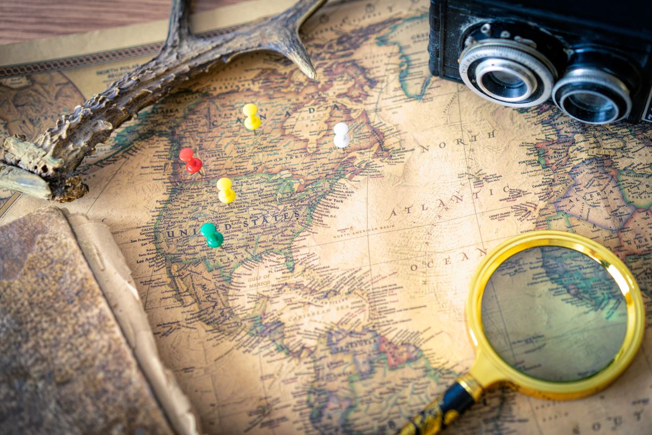 A vintage map with a magnifying glass, camera, and pushpins indicating travel planning.
