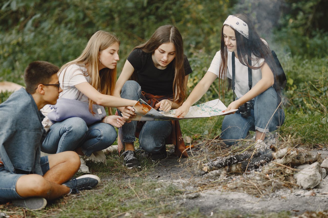 hero-img-02 Group of teens sitting around a campfire, planning adventure with a map.